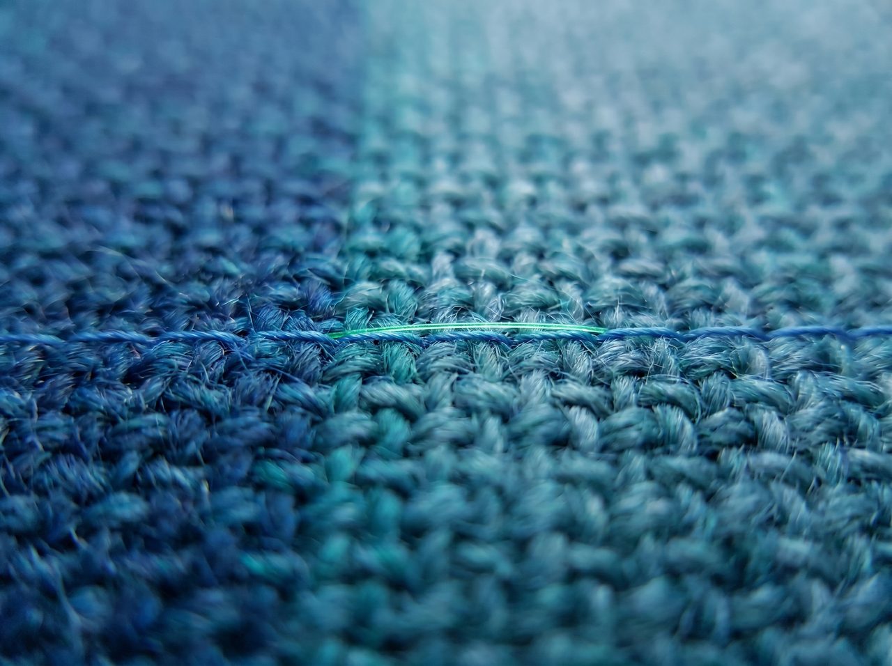 Macro weave of fabric shifting from blue to teal with a single green data thread running through it